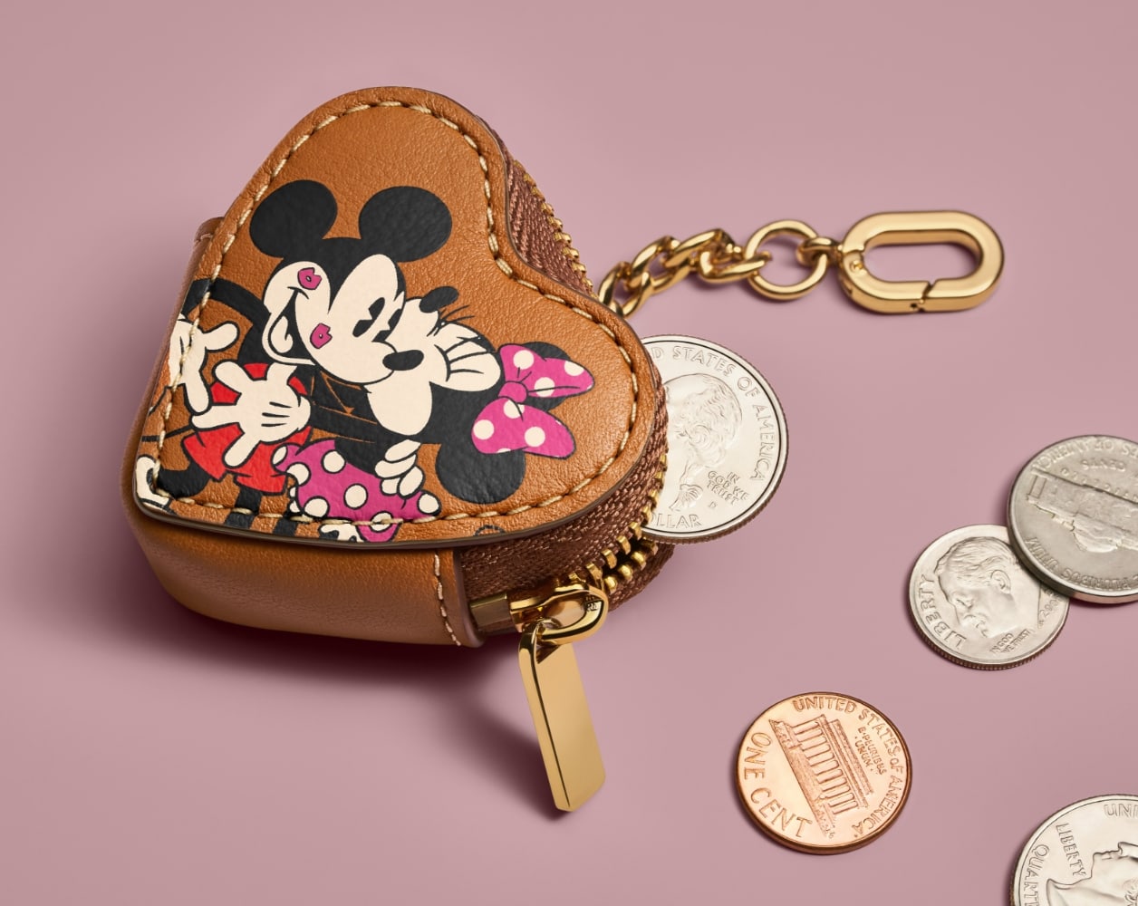 Le porte-monnaie en cuir brun en forme de cœur, marqués à l’effigie de Mickey et Minnie, contenant et cerné de pièces de monnaie.