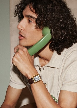 A man wearing the brown leather Carraway watch and holding a green phone receiver. 
