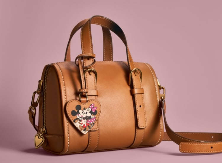 Le mini-sac double porté Carlie en cuir brun présente un détail en forme de cœur en plus d’être marqué à l’effigie de Mickey et Minnie.