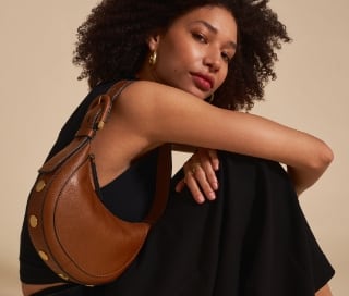 Una mujer con un vestido negro y un bolso Harwell de piel en color marrón.