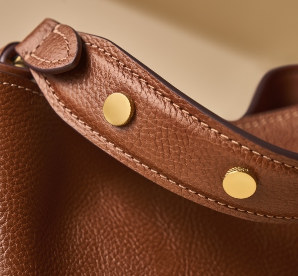 Le bracelet en cuir marron doté de rivets dorés met en valeur la texture subtile de notre Signature Knurling.